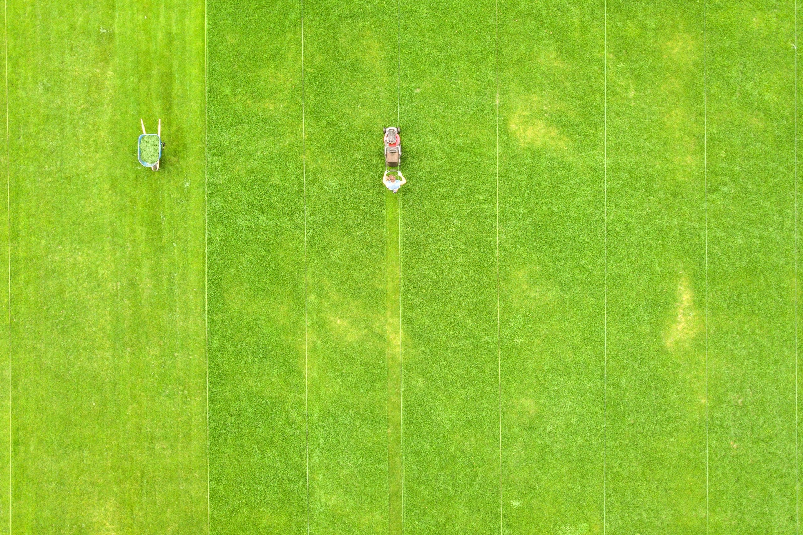 Aerial view of small figure of man worker trimming green grass with mowing machine on football stadium field in Johnston, RI, in summer.