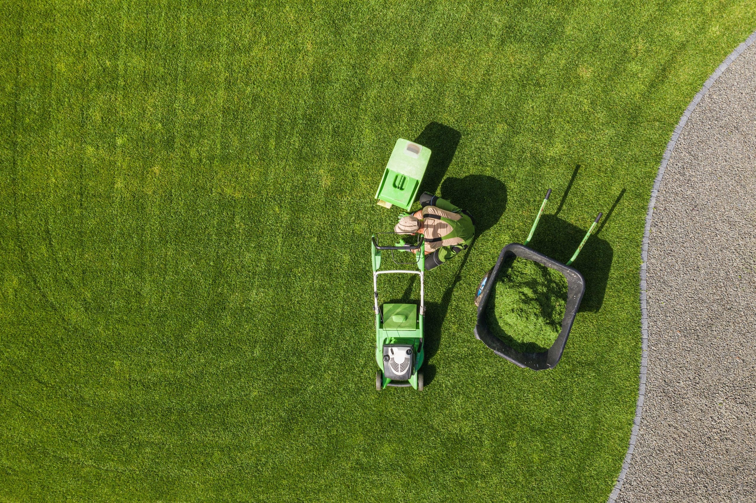 Aerial View of Backyard Garden in Johnston, RI, Lawn Mowing and Weekly Maintenance. Caucasian Gardener in His 40s with Modern Mower Removing Trimmed Grass From the Field.