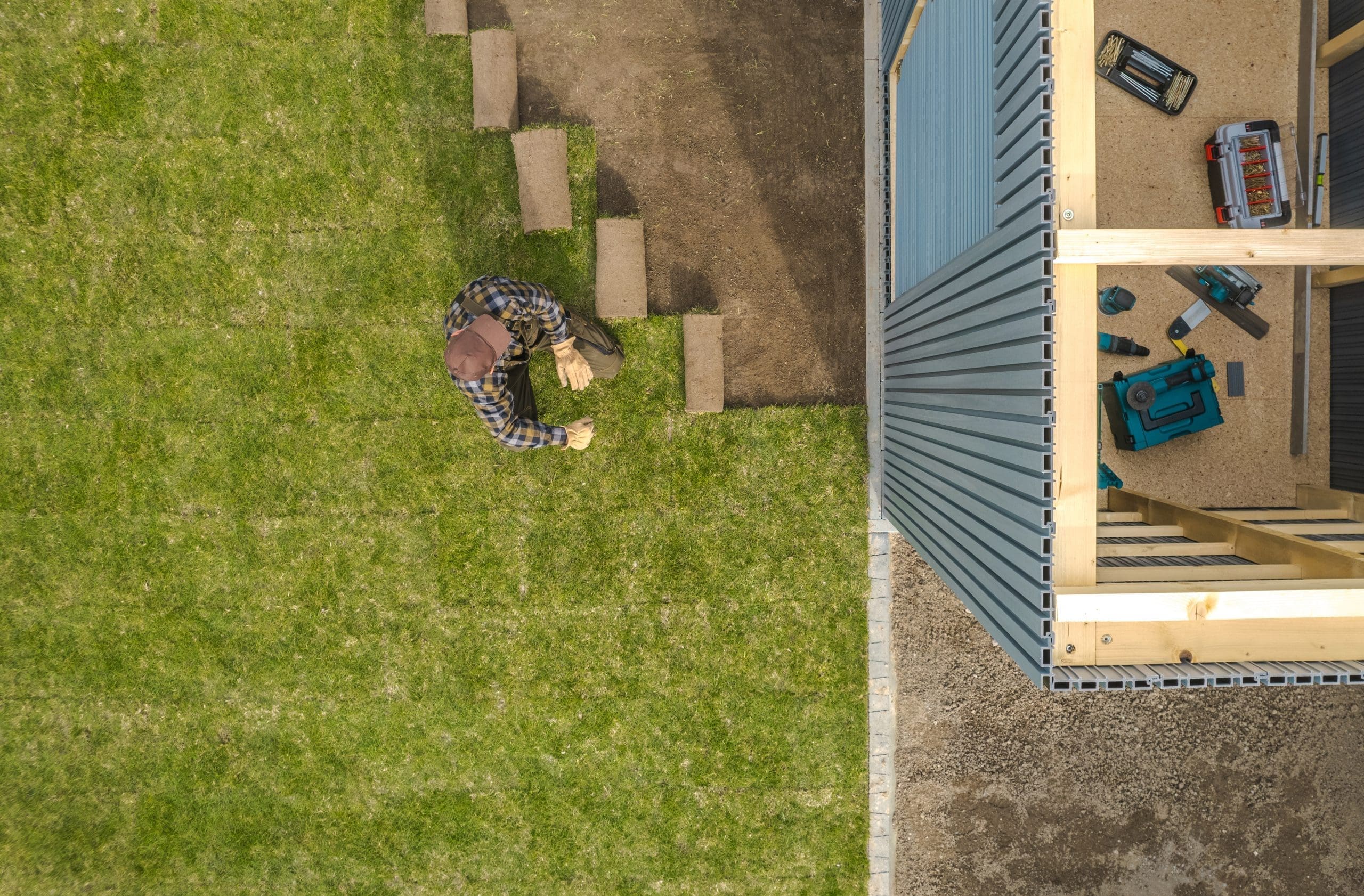 Professional Landscaping Worker Installing Nature Grass Turfs Next to Developed Shed House in a Backyard Garden. Residential Environment.