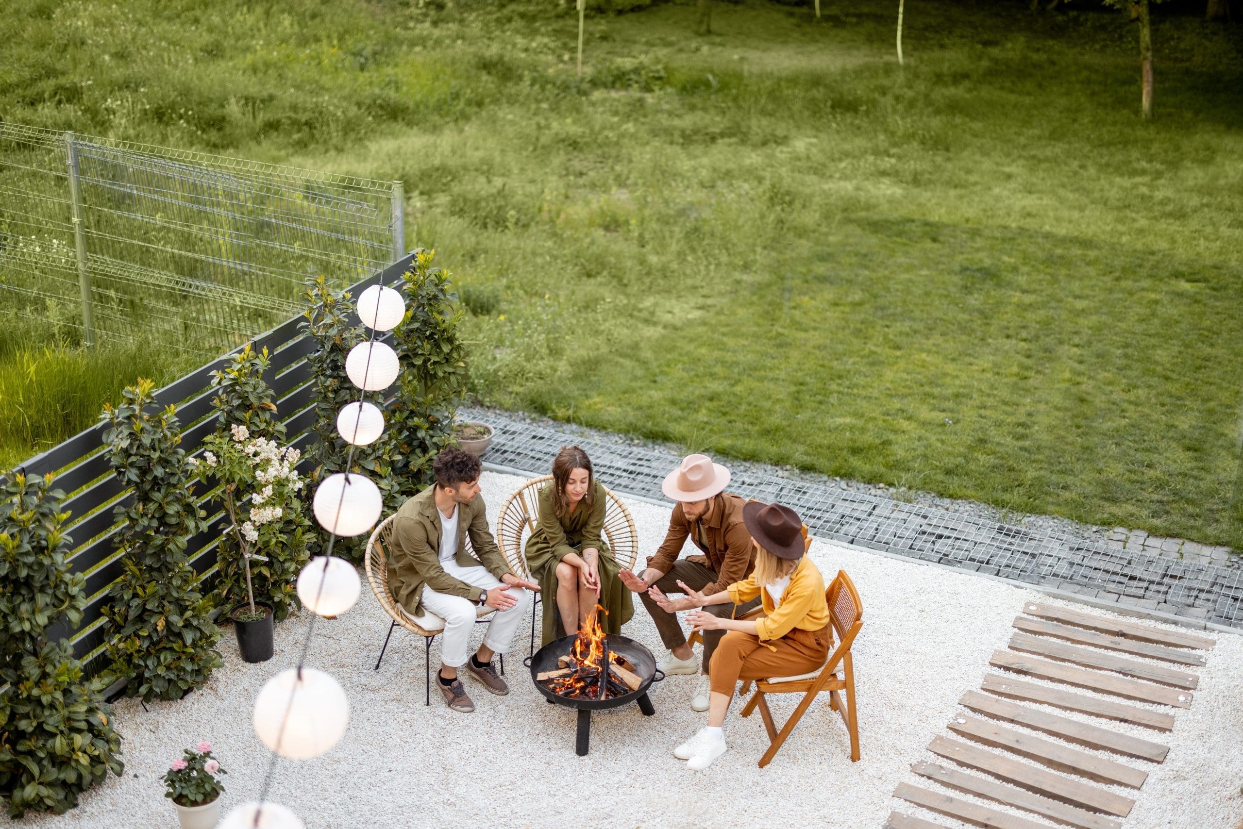 A group of young friends having great summertime, sitting by a fireplace at the backyard of the country house in nature. Top view