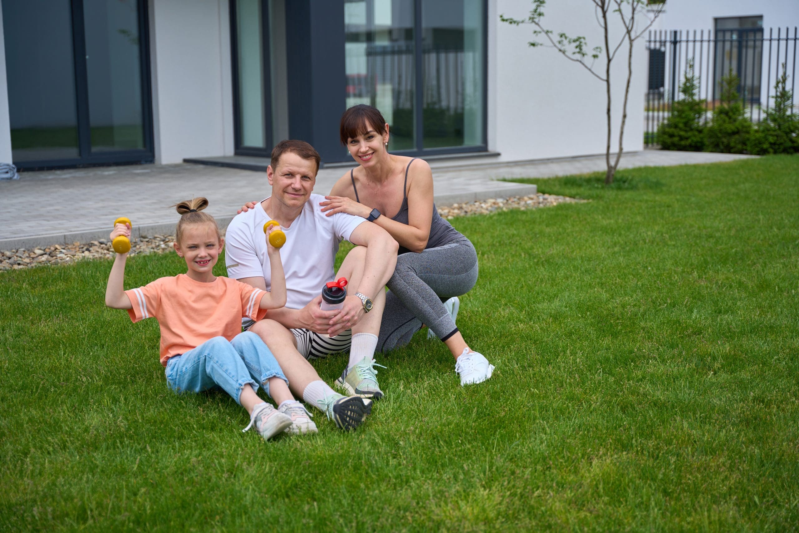 Family Sitting Together on a Lush Green Lawn Mother, father, and daughter sitting on grass that feels spongy when you walk on it